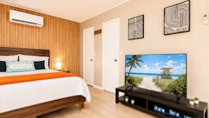 Une chambre à coucher comprenant un lit, un climatiseur, un téléviseur posé sur un meuble et un mur orné de tableaux.