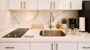 Une cuisine moderne avec des meubles blancs, un évier en acier inoxydable, une machine à café et une bouilloire.
