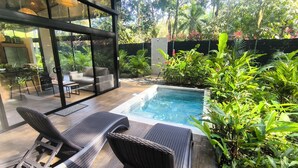 Un espace piscine extérieur moderne, doté de chaises longues, d’un patio fermé par des baies vitrées et d’une végétation luxuriante.