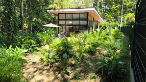 Une maison moderne à la façade en verre, entourée d’une végétation luxuriante.