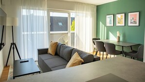 Un salon moderne avec un canapé, une table à manger et des chaises. On peut voir un trépied et une télécommande sur une table.