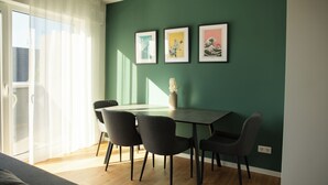 Un coin repas avec une table et des chaises, un vase rempli de fleurs et trois tableaux encadrés accrochés au mur.
