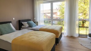 Une chambre d’hôtel avec deux lits, une fenêtre avec des rideaux, une vue sur l’extérieur et une petite table sur laquelle est posé un vase.