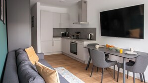 Une cuisine moderne avec des armoires blanches, une hotte en acier inoxydable et un téléviseur à écran plat fixé au mur.