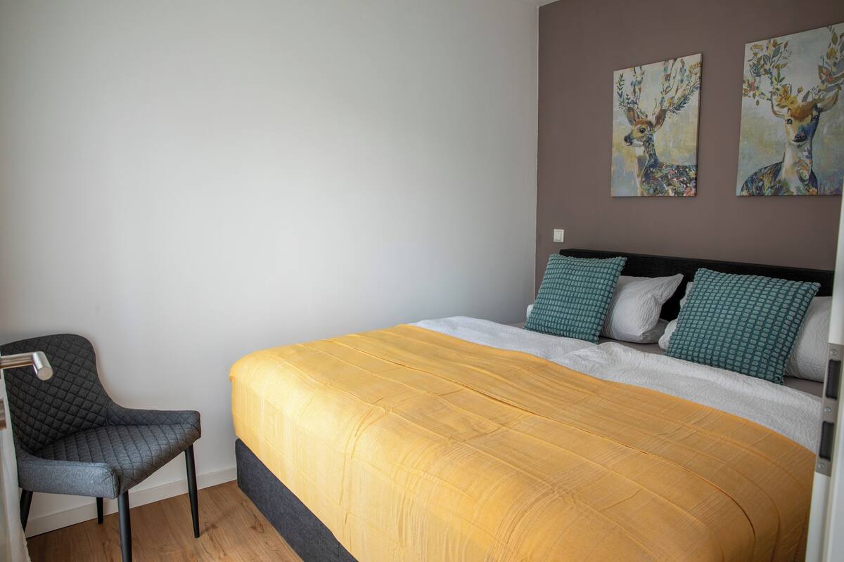 Un dormitorio con una cama, una silla y dos cuadros en la pared.