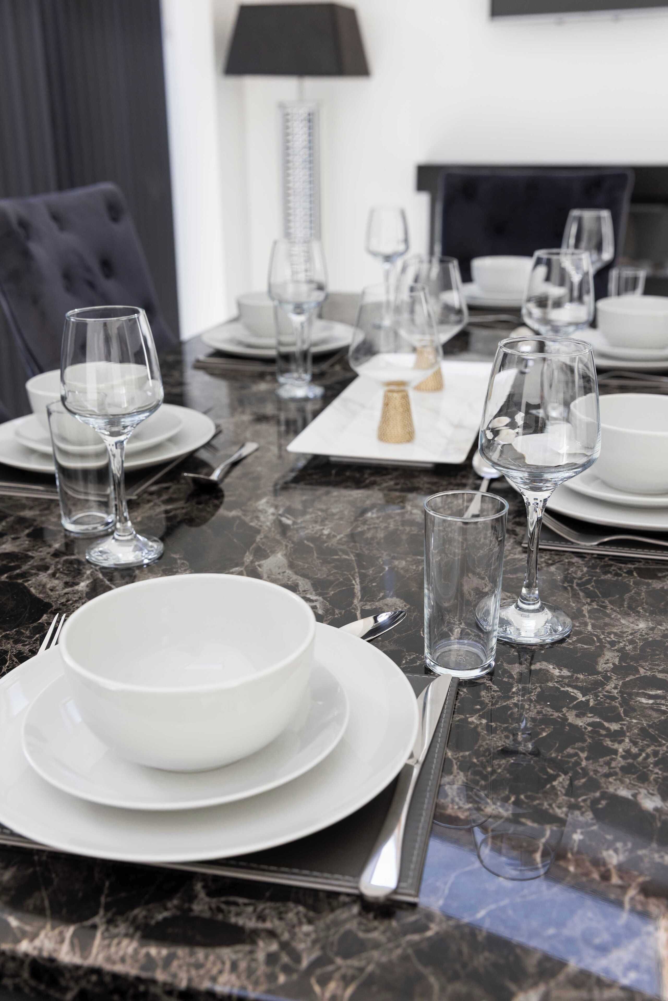 A dining table set with plates, bowls, cutlery, and wine glasses.