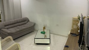 A living room with a grey sofa, a glass coffee table, a TV stand with a TV, and an air conditioner on the wall. - Centrally located apartment, close to airport, beaches and historical center. (Cartagena de Indias)
