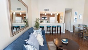 Ein modernes Wohnzimmer mit einem blauen Sofa, einem Esstisch und einer Küchenzeile mit Barhocker.