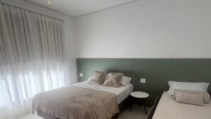 A modern hotel room with a large bed, a smaller bed, a bedside table, and a window with curtains. - Duplex Penthouse with Jacuzzi and Views of 2 Beaches (Bombinhas)