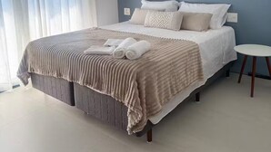 A modern bedroom with a large bed, a painting of a sailboat, and a view of the sea through sheer curtains. - Duplex Penthouse with Jacuzzi and Views of 2 Beaches (Bombinhas)