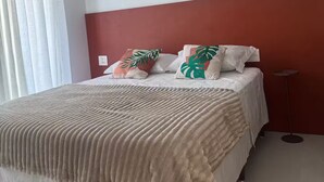 A bed with a textured blanket, two pillows with tropical leaf designs, a red accent wall, and a standing floor lamp. - Duplex Penthouse with Jacuzzi and Views of 2 Beaches (Bombinhas)
