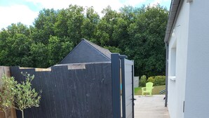 Een omheind gebied met een houten terras, een bloempot en een wit gebouw op de achtergrond.