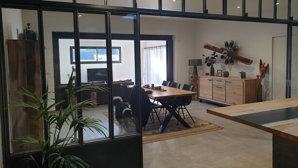 Een moderne woonkamer met een eethoek, grote ramen en een trap.