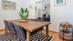 Un espace de salle à manger moderne avec une table en bois, des chaises à revêtement gris, un tapis à rayures et une petite table d'appoint en osier.