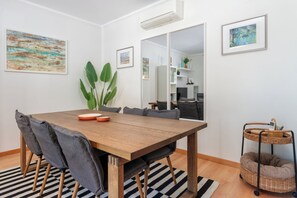 Uma sala de jantar moderna com mesa de madeira, cadeiras estofadas cinzentas, tapete listrado e mesa auxiliar de vime.
