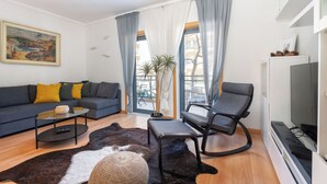 Un salon moderne comprenant un canapé, une table basse, un fauteuil, un téléviseur et une grande fenêtre avec des rideaux.
