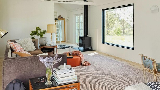 A cozy living room with a sofa, a coffee table, a fireplace, and a large window. - Converted 1800s stable near Kalmarsund (Söderåkra)