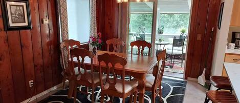 A wooden-paneled room with a dining table and chairs, a chandelier, and a patterned rug.