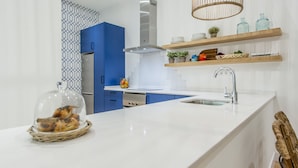 Eine moderne Küche mit weißer Arbeitsplatte, blauen Schränken und einer Edelstahl-Dunstabzugshaube. Darüber befinden sich Holzregale mit verschiedenen Küchenutensilien.