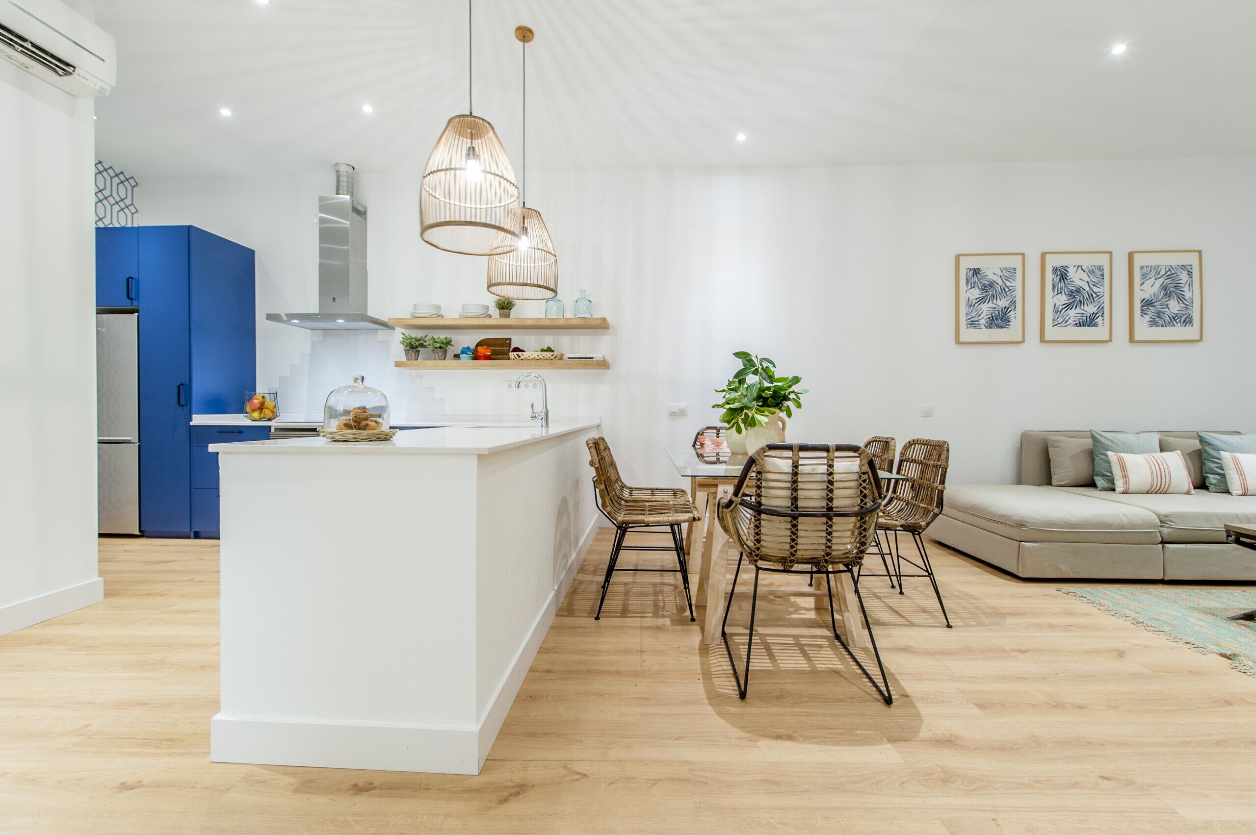 A modern kitchen with a central island, blue cabinets, and a dining area with wicker chairs.