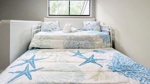 A bed with a starfish and coral pattern bedspread, a window with a view of trees, and a white headboard.