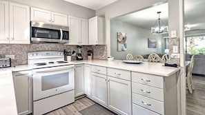 Una cocina moderna con armarios blancos, microondas integrado, estufa y un comedor con vistas.