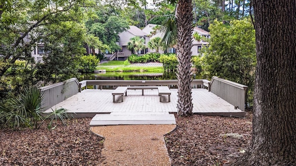 A wooden deck with benches, surrounded by trees and a body of water.