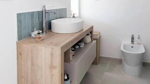 Un baño moderno con un tocador de madera, un espejo grande, un lavabo redondo y un bidé.