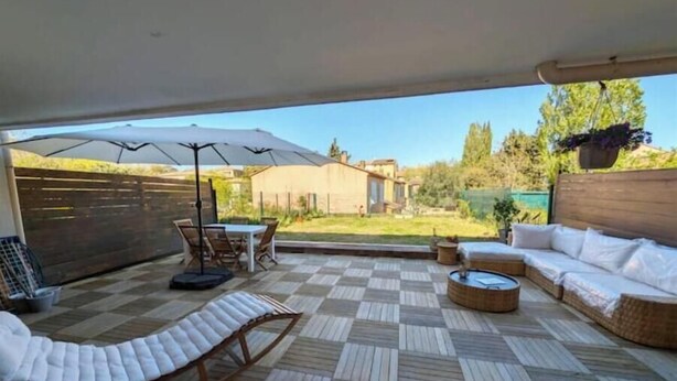 Un patio al aire libre con una mesa de comedor, sillas, una silla de lounge, un sofá y un paraguas grande.