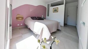 Un dormitorio con cama, lámpara de pared, puerta y un pequeño cuadro enmarcado.