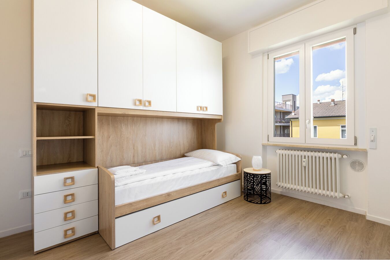 A bedroom with a bed, built-in storage, a radiator, and a window with a view.