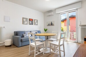 Ein modernes Wohnzimmer mit einem blauen Sofa, weißen Sesseln, einem Holztisch und einem Balkon mit Blick.