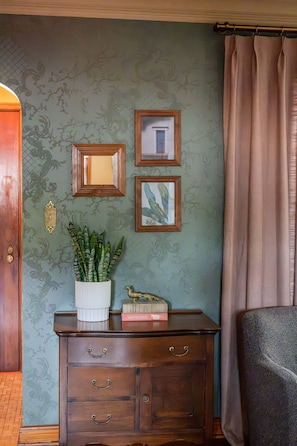 A room with a patterned wallpaper, a wooden cabinet with drawers, a potted plant, and framed pictures on the wall. - Walnut Row, Walk to Valley Junction,  Sleeps 10+ (West Des Moines)