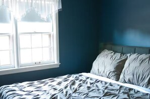 A bedroom with a bed, a window, and a blue wall. - Walnut Row, Walk to Valley Junction,  Sleeps 10+ (West Des Moines)