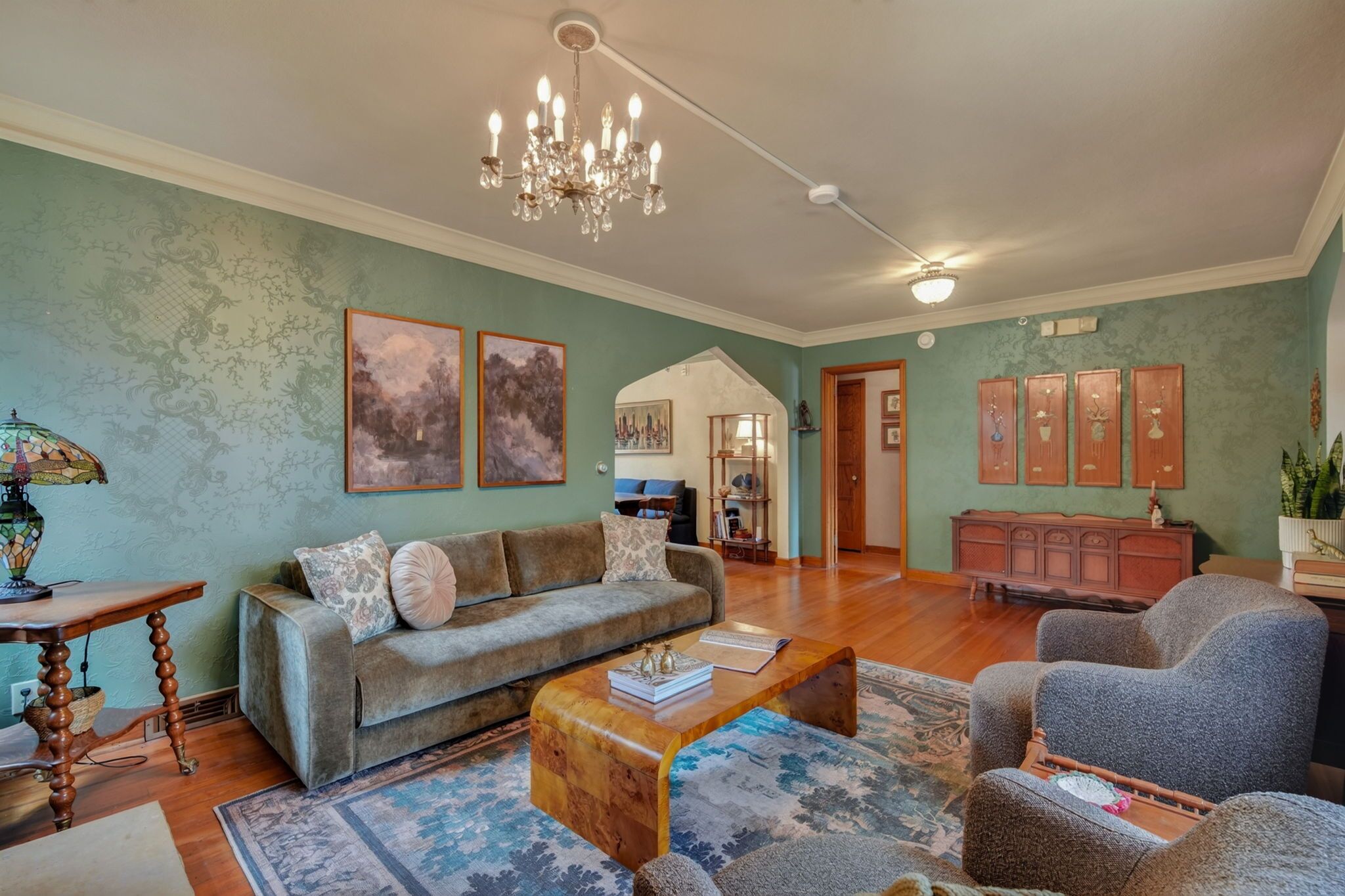 A spacious living room with a sofa, armchairs, a coffee table, and a chandelier.