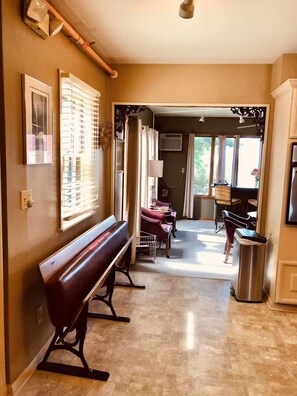 A hallway with a bench, a trash can, and a window with blinds. - Walnut Row, Walk to Valley Junction,  Sleeps 10+ (West Des Moines)