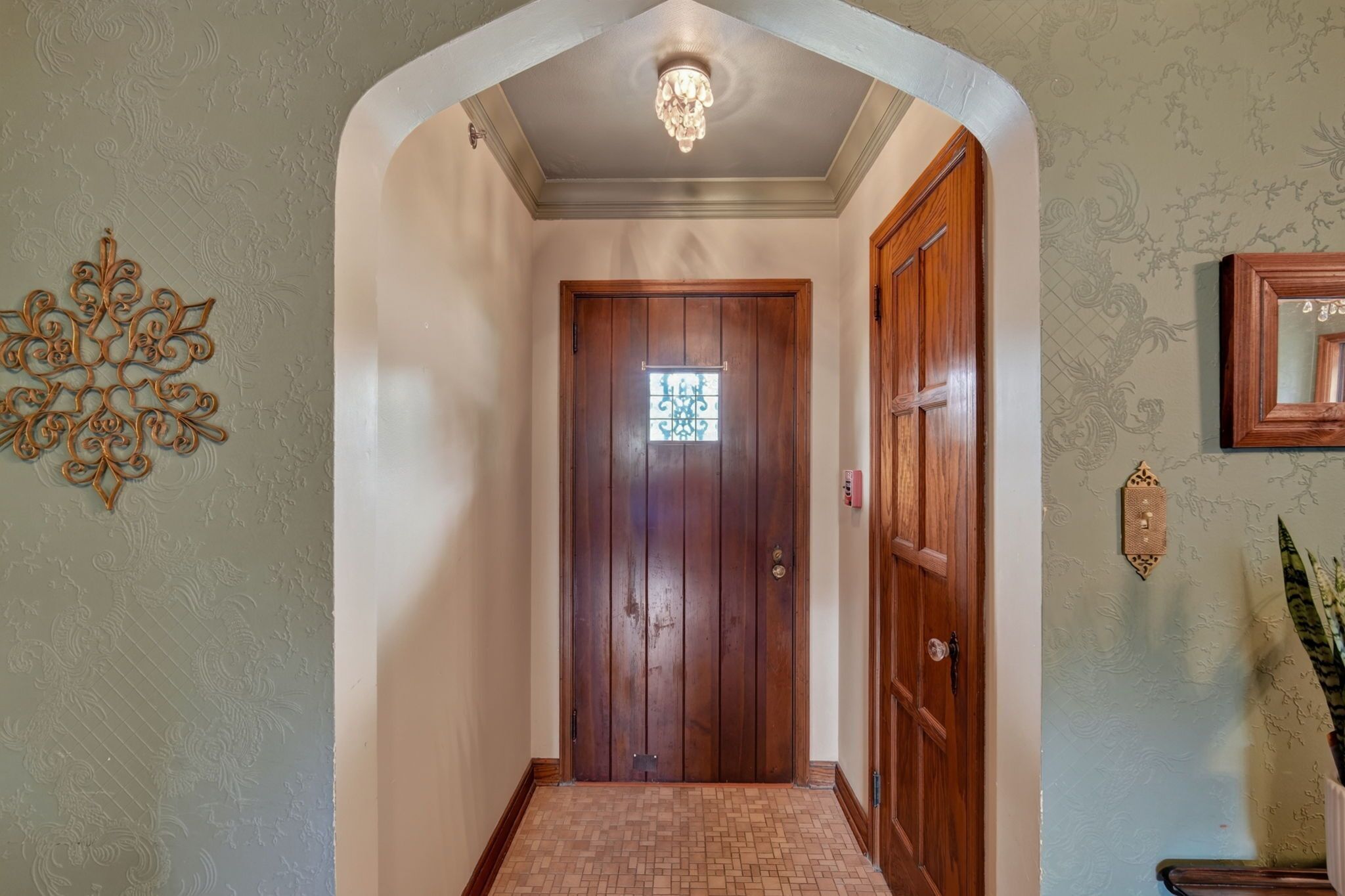 Un couloir avec une porte en bois, un élément décoratif mural et un miroir encadré.