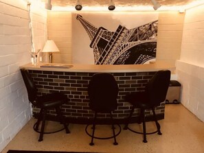 A reception area with a brick counter, two black chairs, a white lamp, and a large black and white artwork of a bridge. - Walnut Row, Walk to Valley Junction,  Sleeps 10+ (West Des Moines)