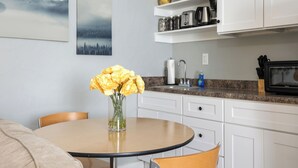 Une cuisine avec des meubles blancs, un plan de travail en granit et un vase rempli de fleurs jaunes, posé sur une table ronde.