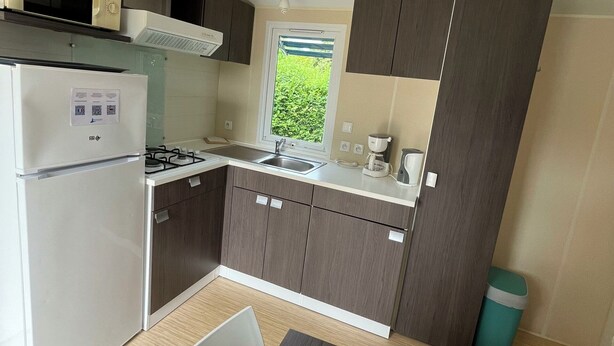 Uma cozinha compacta com geladeira, fogão, micro-ondas e janela com vista para o verde.