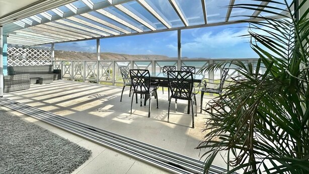 Eine überdachte Terrasse mit Tisch und Stühlen, Blick auf die Landschaft und einer Pflanze.