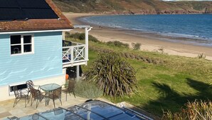 Ein Küsteneigentum mit einem blauen Gebäude, einer Terrasse mit Stühlen und einem Tisch sowie Blick auf Strand und Meer.