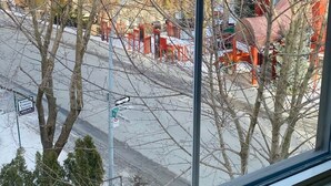 A window view of a street with bare trees, a red building, and a street sign. - Les Ancestrales - Maison Turcot Art Déco (Saint-Hyacinthe)