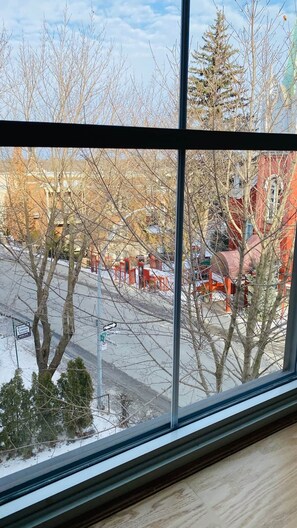 A window view of a street with bare trees, a red building, and a street sign.