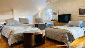 A room with two beds, a round wooden stool, a TV, and a brick wall. - Les Ancestrales - Maison Turcot Art Déco (Saint-Hyacinthe)