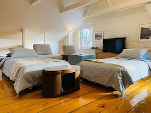 A room with two beds, a round wooden stool, a TV, and a brick wall. - Les Ancestrales - Maison Turcot Art Déco (Saint-Hyacinthe)