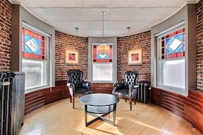 Una habitación con paredes de ladrillo, dos sillones de cuero, una mesa redonda y ventanas grandes con vidrieras.