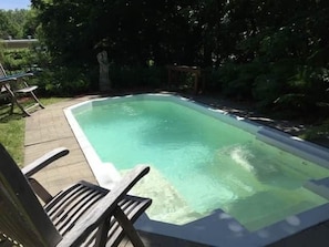 A rectangular swimming pool with a wooden deck and chairs, surrounded by greenery. - Les Ancestrales - Suite romantique (Saint-Hyacinthe)