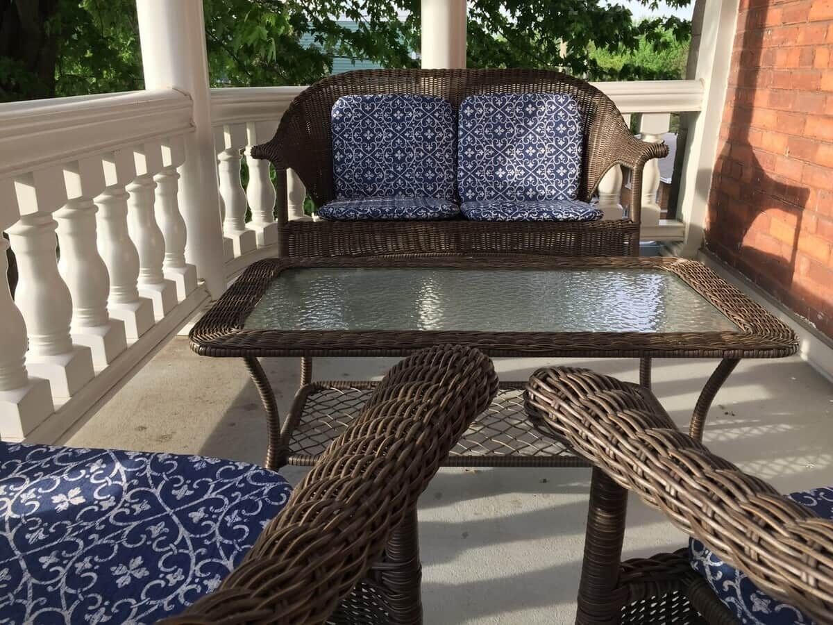 A wicker outdoor seating area with a glass-top table, white balustrade, and patterned cushions.