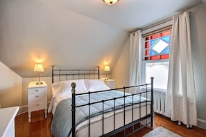 A bedroom with a metal bed frame, two bedside tables with lamps, a window with curtains, and a radiator. - Les Ancestrales - Suite romantique (Saint-Hyacinthe)